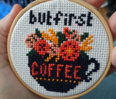 Hand-stitched embroidery hoop with flowers and the phrase "but first, coffee."